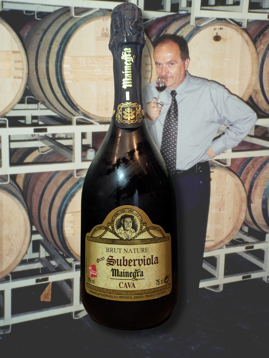 Bottle of Mainegra Gran 'Suberviola' Brut Cava NV in front of a winemaker and barrels. Crisp, clean label with traditional cava elegance.