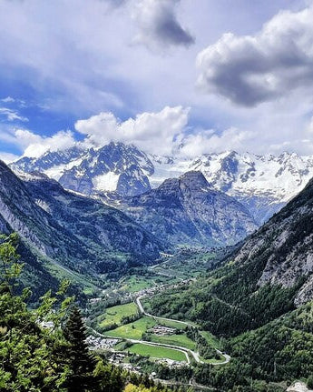 Valley surrounded by mountains with snow-capped peaks under a blue sky with clouds.