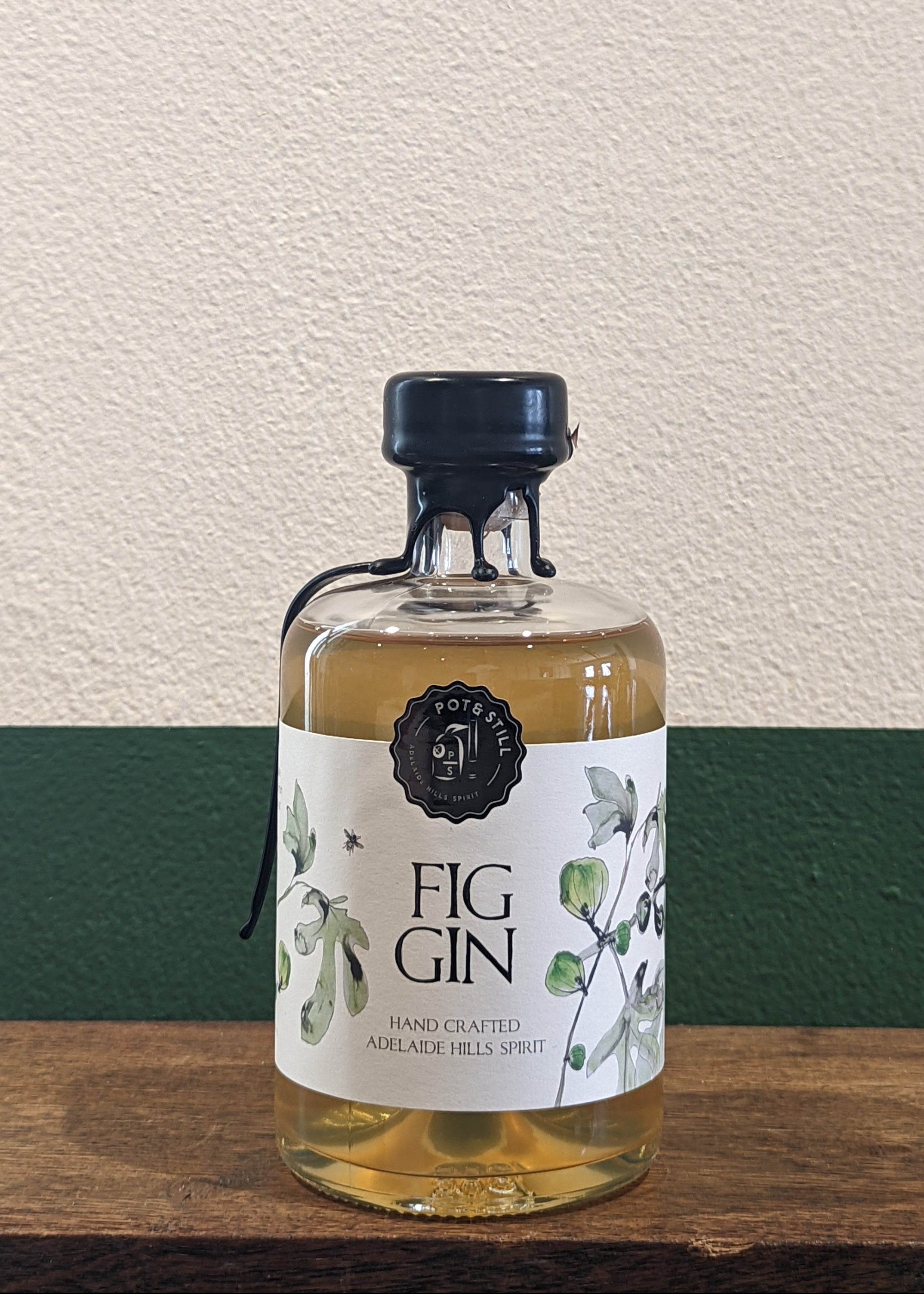 A bottle of Pot & Still Fig Gin placed on a wooden surface with a plain wall in the background.